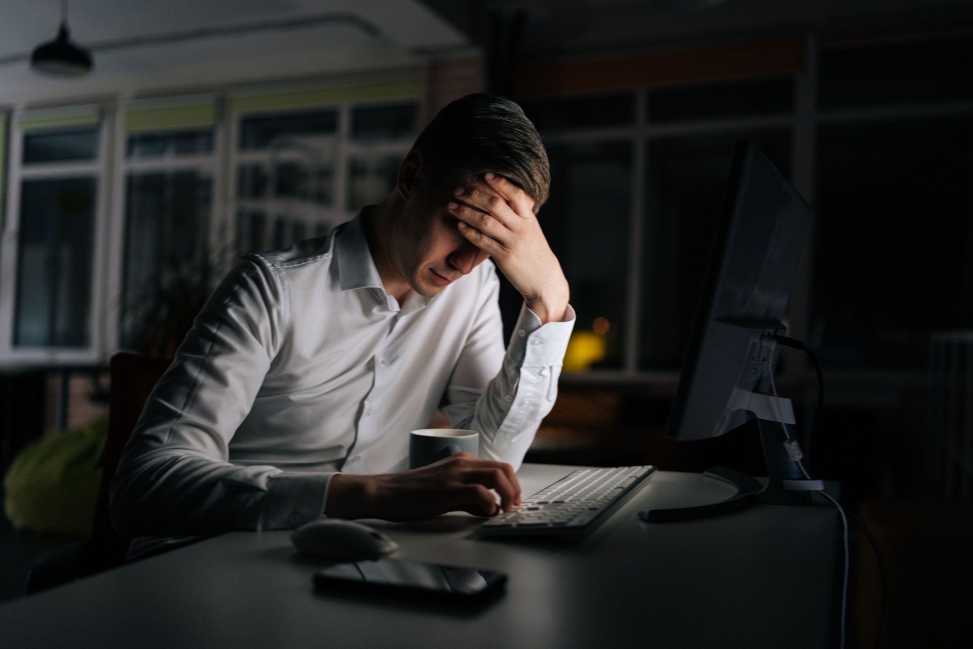 Exhausted businessman working in evening office alone. Tired anxious manager losing failure working on computer at late night. Tired worried business man at workplace